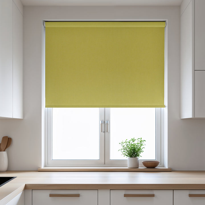 Yellow roller blind on a window in a kitchen with white cabinets and a plant on the windowsill.