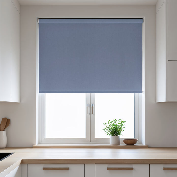 Blue roller blind on a window in a kitchen with white cabinets and a plant on the windowsill.