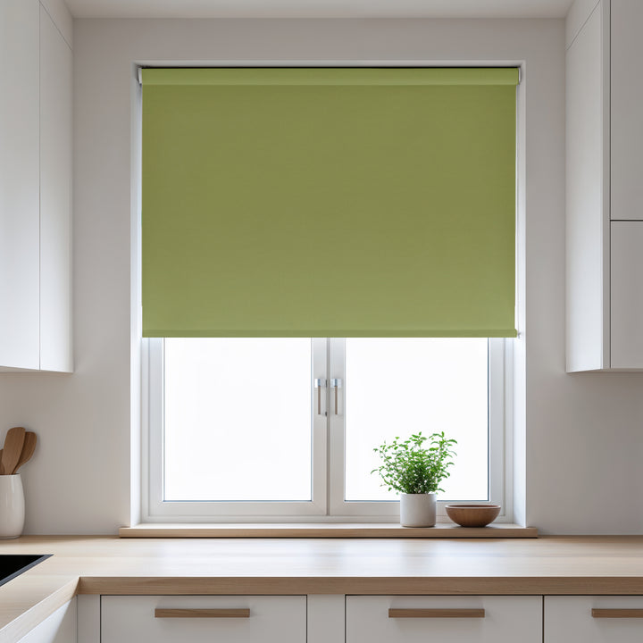 Green roller blind on a window in a kitchen with white cabinets and a plant on the windowsill.