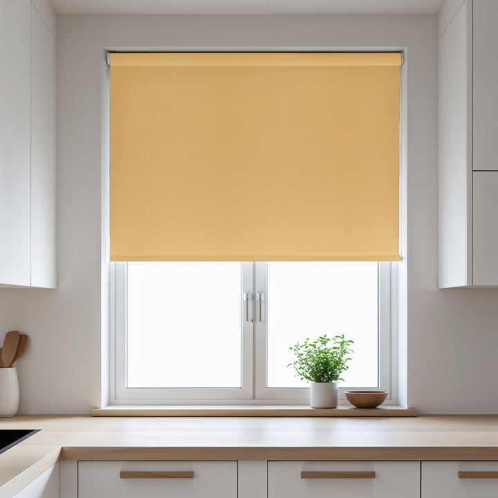 Yellow roller blind on a window in a kitchen with white cabinets and a plant on the windowsill.