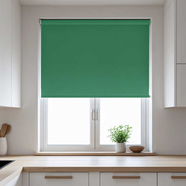 Green roller blind on a window in a kitchen with white cabinets and a plant on the windowsill.