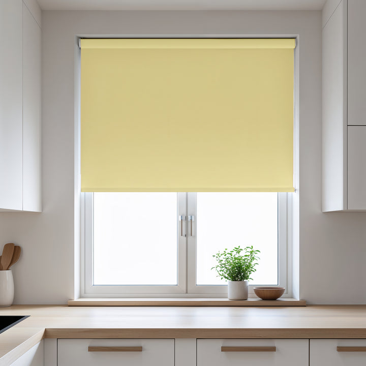 Yellow roller blind on a window in a kitchen with white cabinets and a plant on the windowsill.