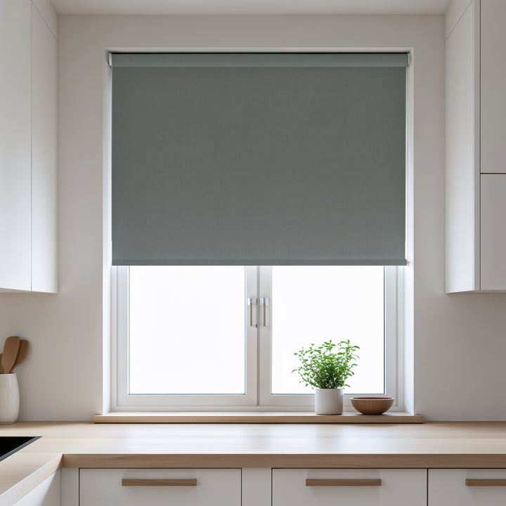 Gray roller blind covering a window in a kitchen with light-colored walls and wooden countertops.