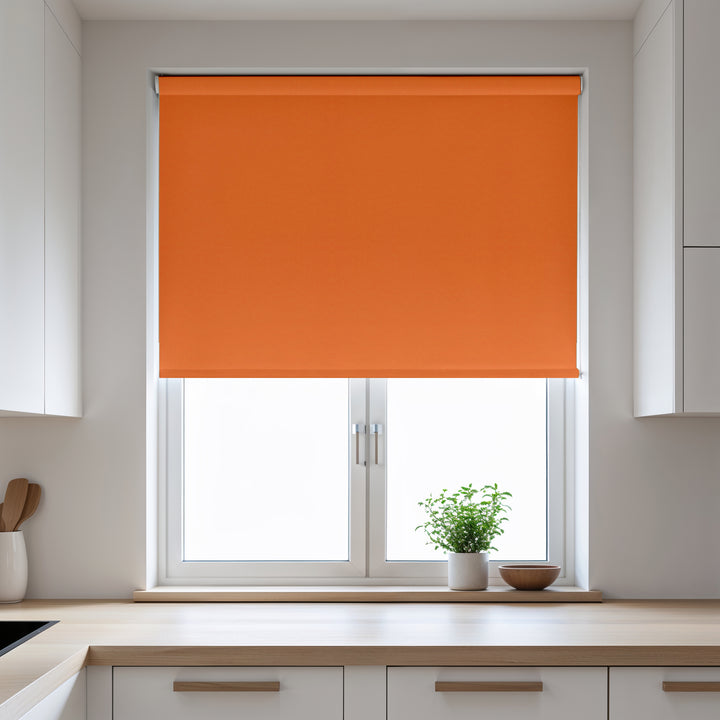 Orange roller blind on a window in a kitchen with white cabinets and a plant on the windowsill.